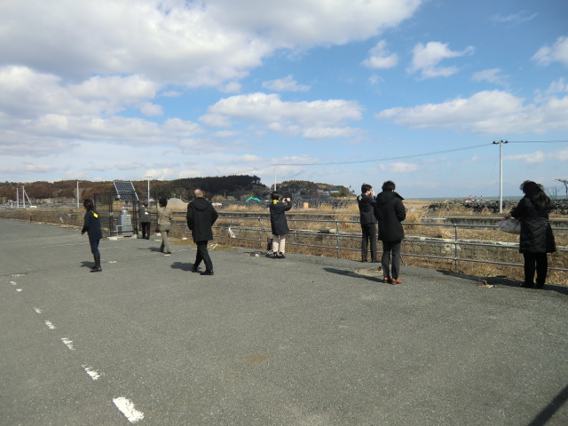 富岡駅跡を見学する参加者。黒いフレコンバッグが積み重なっています。